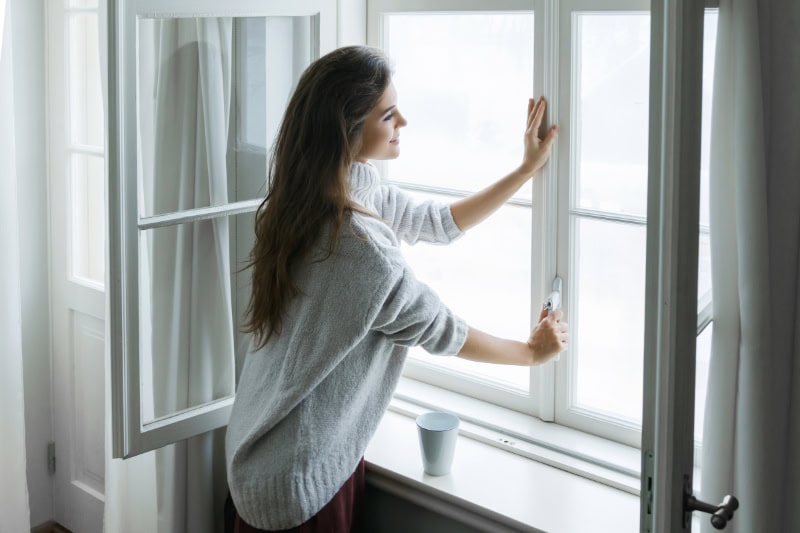 What Is an Air Handler? Photo of a young woman opening her window inside her home.